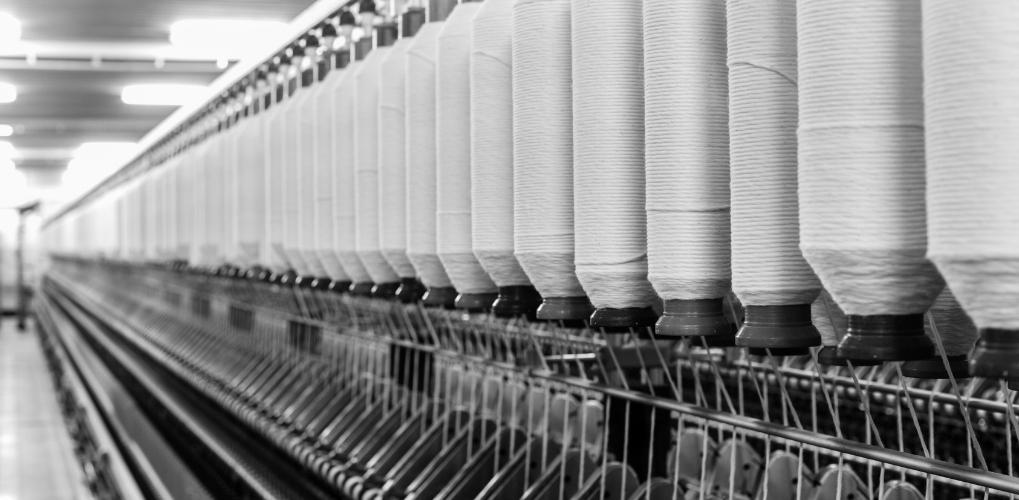 Industrial textile spinning line with aligned spools of thread, a symbol of Italian manufacturing production and quality.